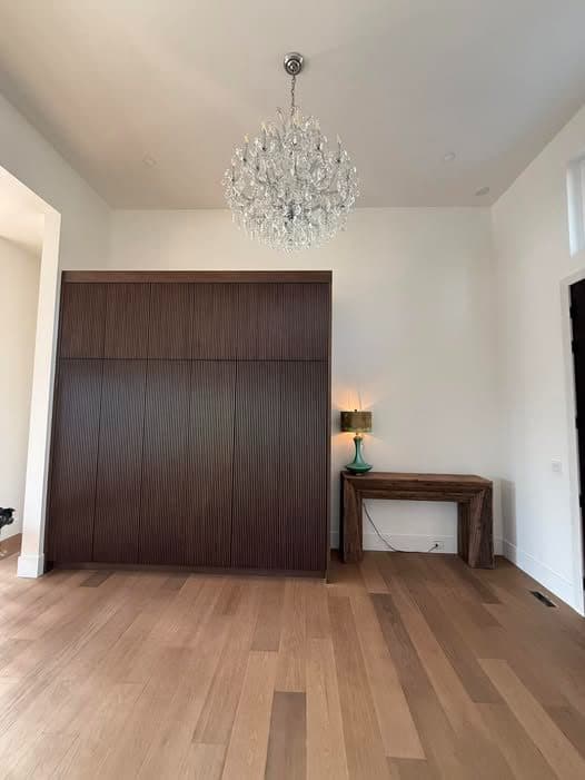 A plain, empty dining room with a large window and light wood floors.